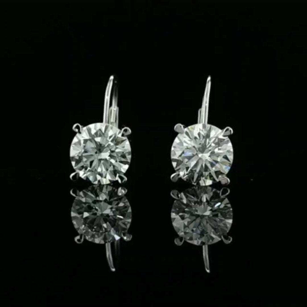 May include: A pair of gold dangle earrings with clear round cubic zirconia stones. The earrings have a hook closure.