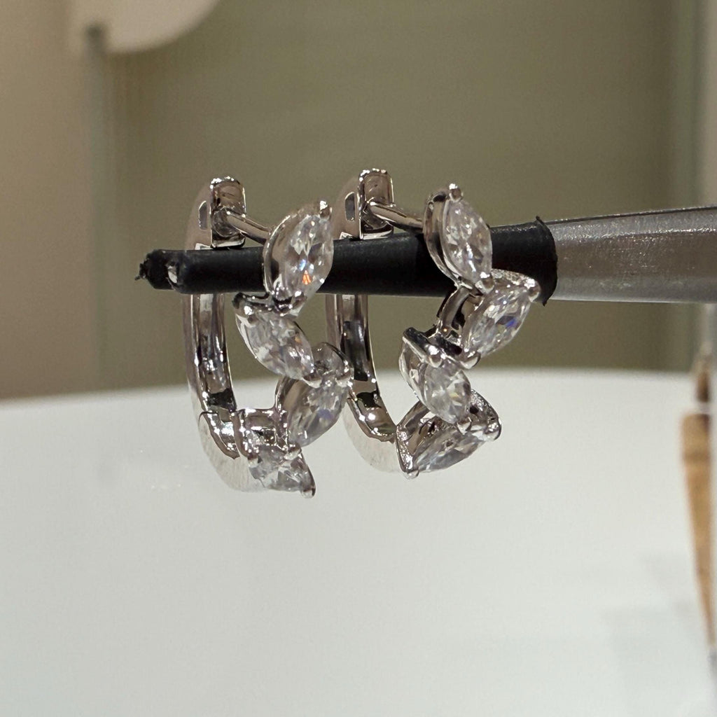 May include: Two white gold hoop earrings with marquise shaped clear diamonds set in a row around the hoop.