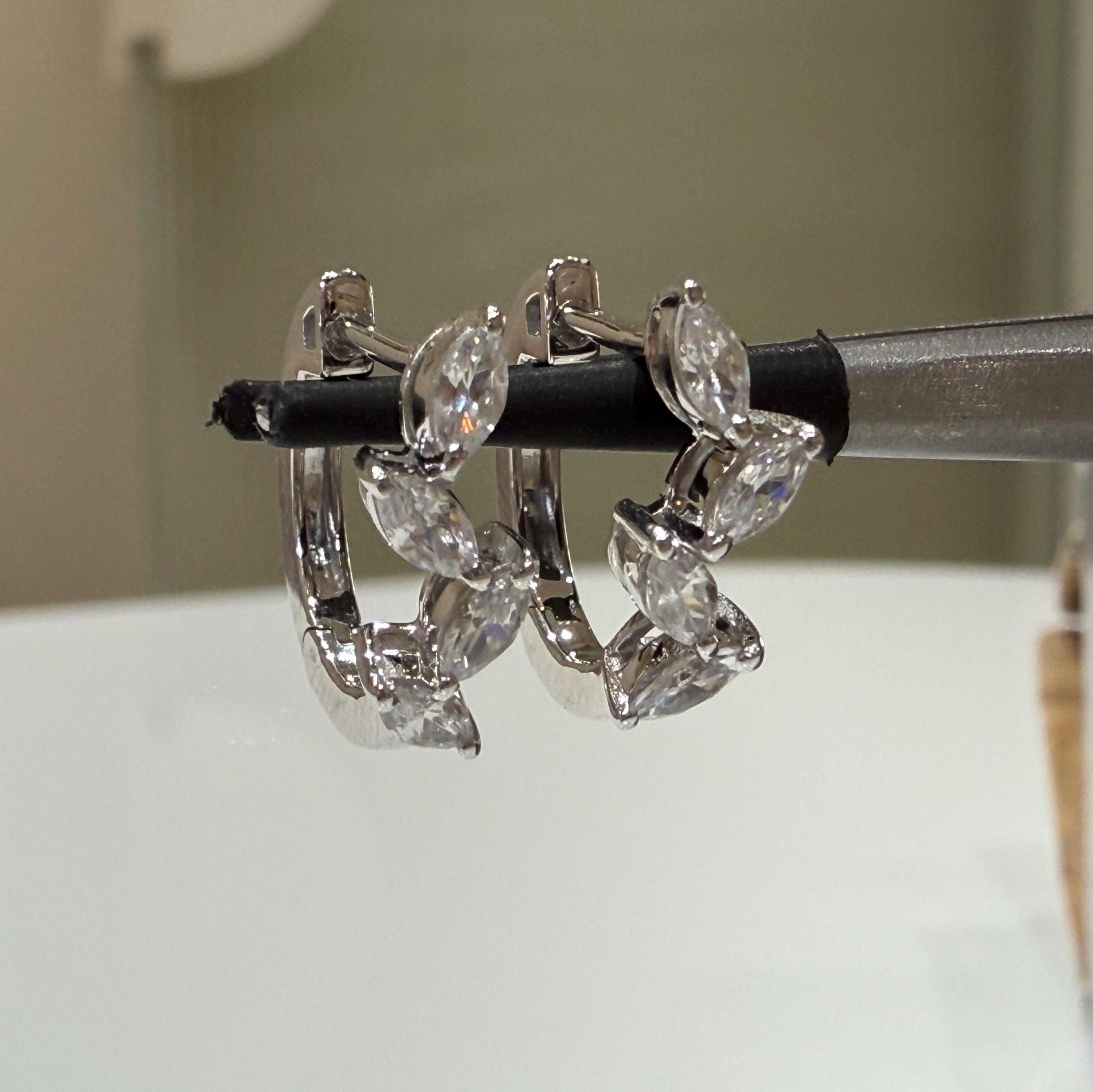 May include: Two white gold hoop earrings with marquise shaped clear diamonds set in a row around the hoop.