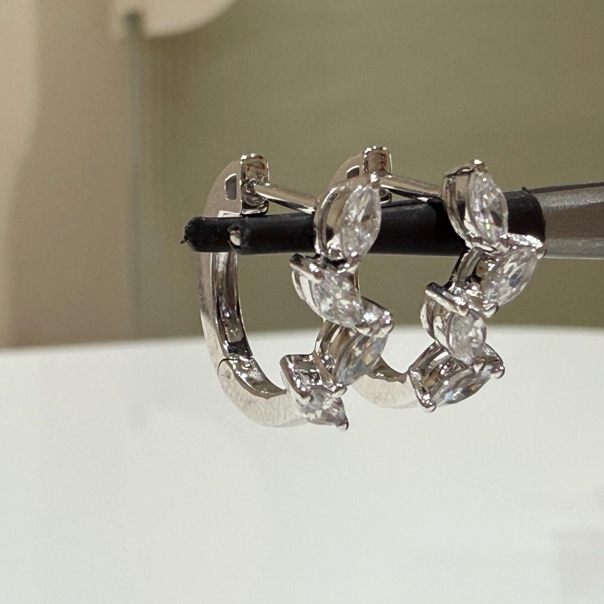 May include: A pair of gold hoop earrings with a row of marquise-shaped clear diamonds around the hoop.