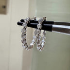 May include: Two gold hoop earrings with a row of clear round gemstones around the hoop.