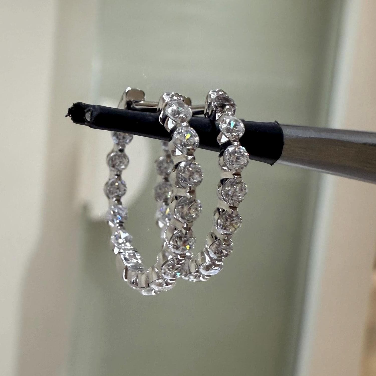 May include: Two gold hoop earrings with a row of small, clear, round gemstones around the outside of each hoop.