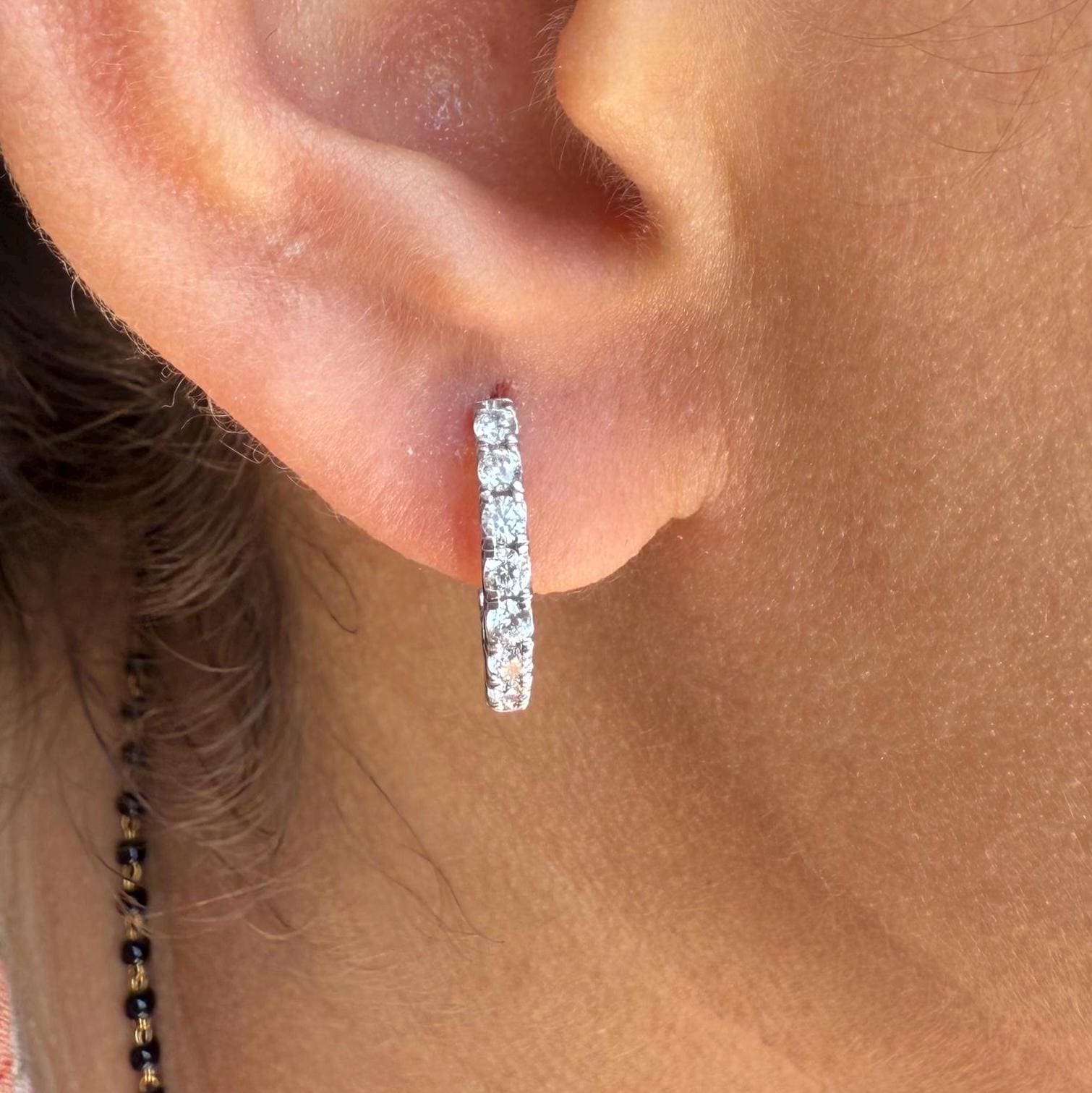 May include: A pair of small gold hoop earrings with a row of clear sparkling stones around the hoop.