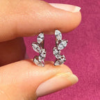 May include: A pair of gold earrings with a leaf design. Each earring has five small, clear, marquise-shaped diamonds set in a row.