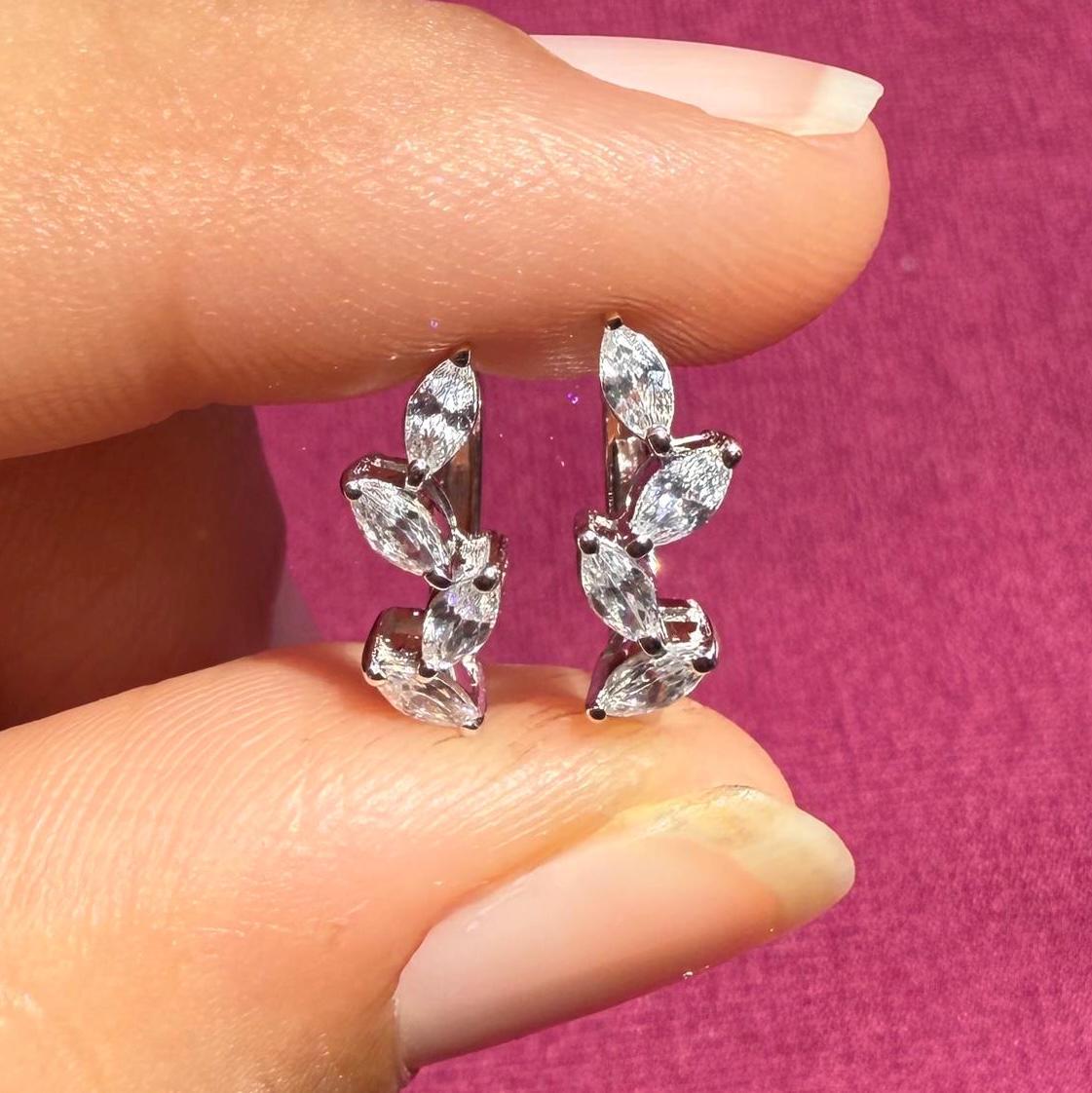 May include: A pair of gold earrings with a leaf design. Each earring has five small, clear, marquise-shaped diamonds set in a row.