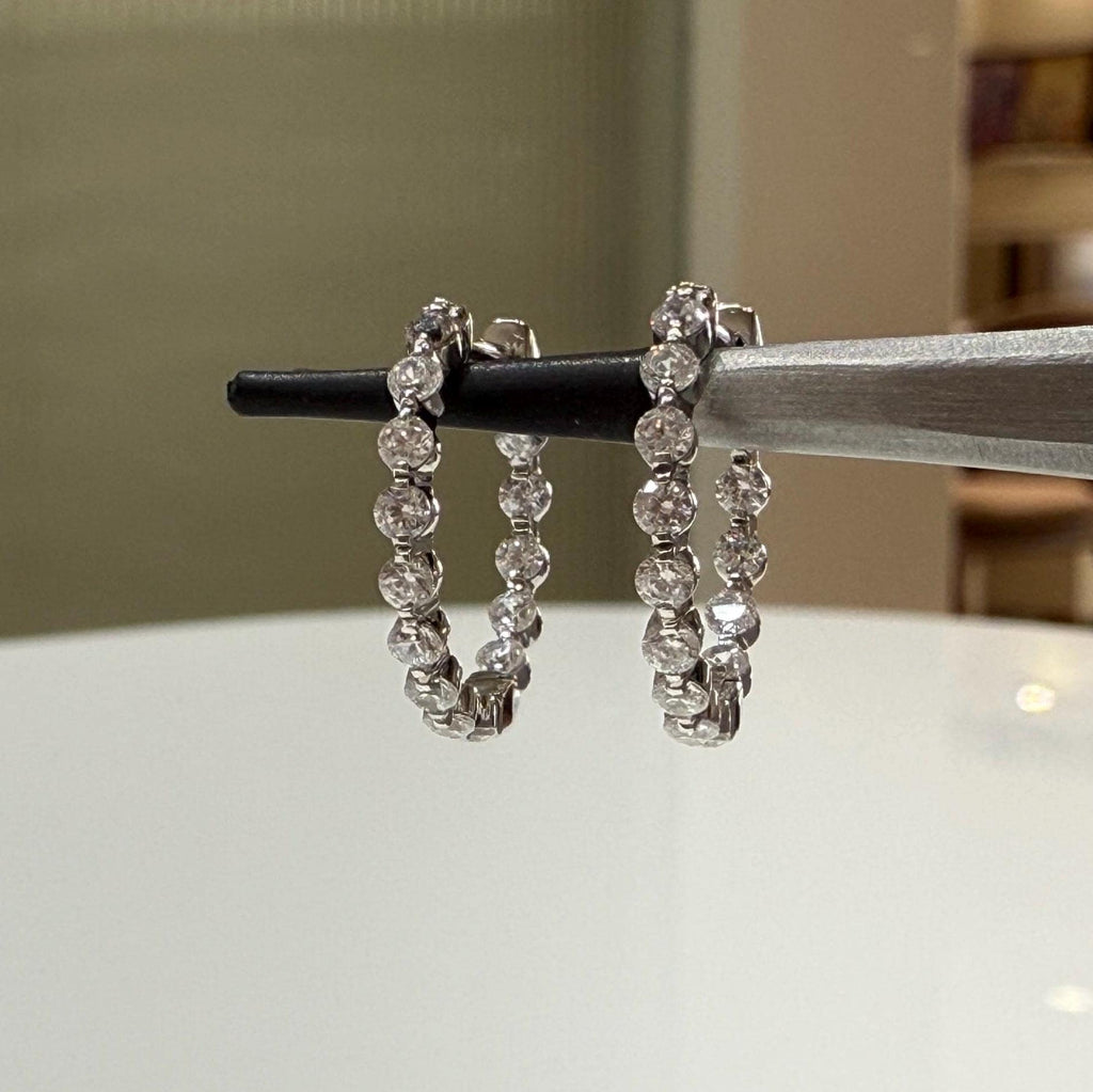 May include: Two white gold hoop earrings with a row of small, clear diamonds around the outside of each hoop.